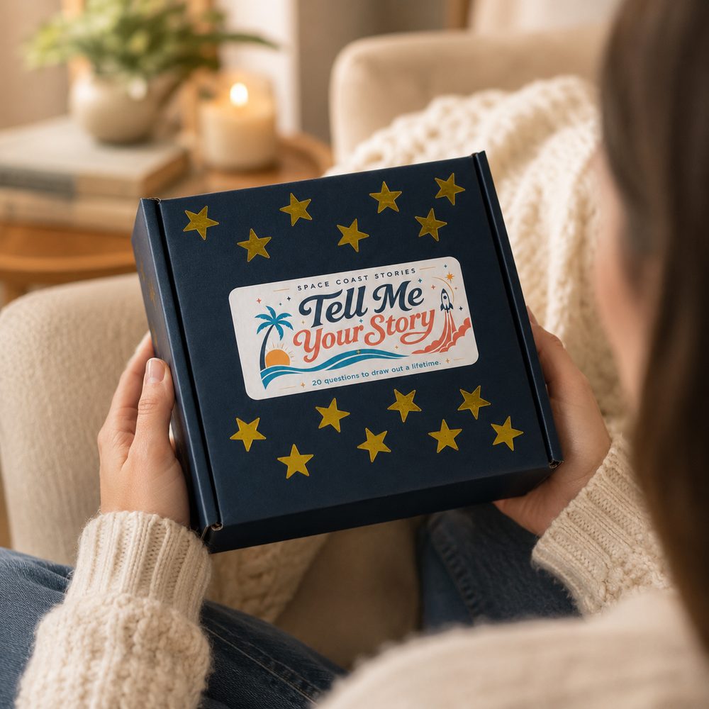 A person holding the navy, gold-star Tell Me Your Story card kit box